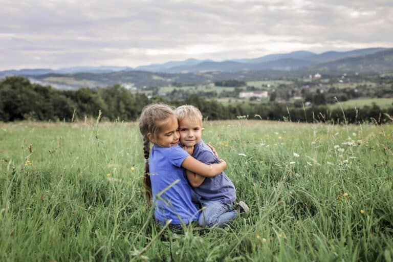 Cute girl hugging her brother sitting on the grass
