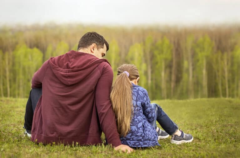 Little girl and her father facing away from the camera sitting on the grass