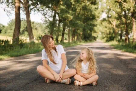 Mom and blonde hair daughter smiling at each other while sitting on road