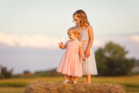 Two adorable sisters standing on a hayfield during sunset hours