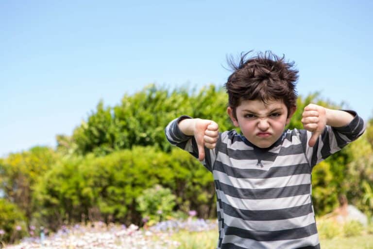 Cute boy looking at the camera showing thumbs down in the countryside